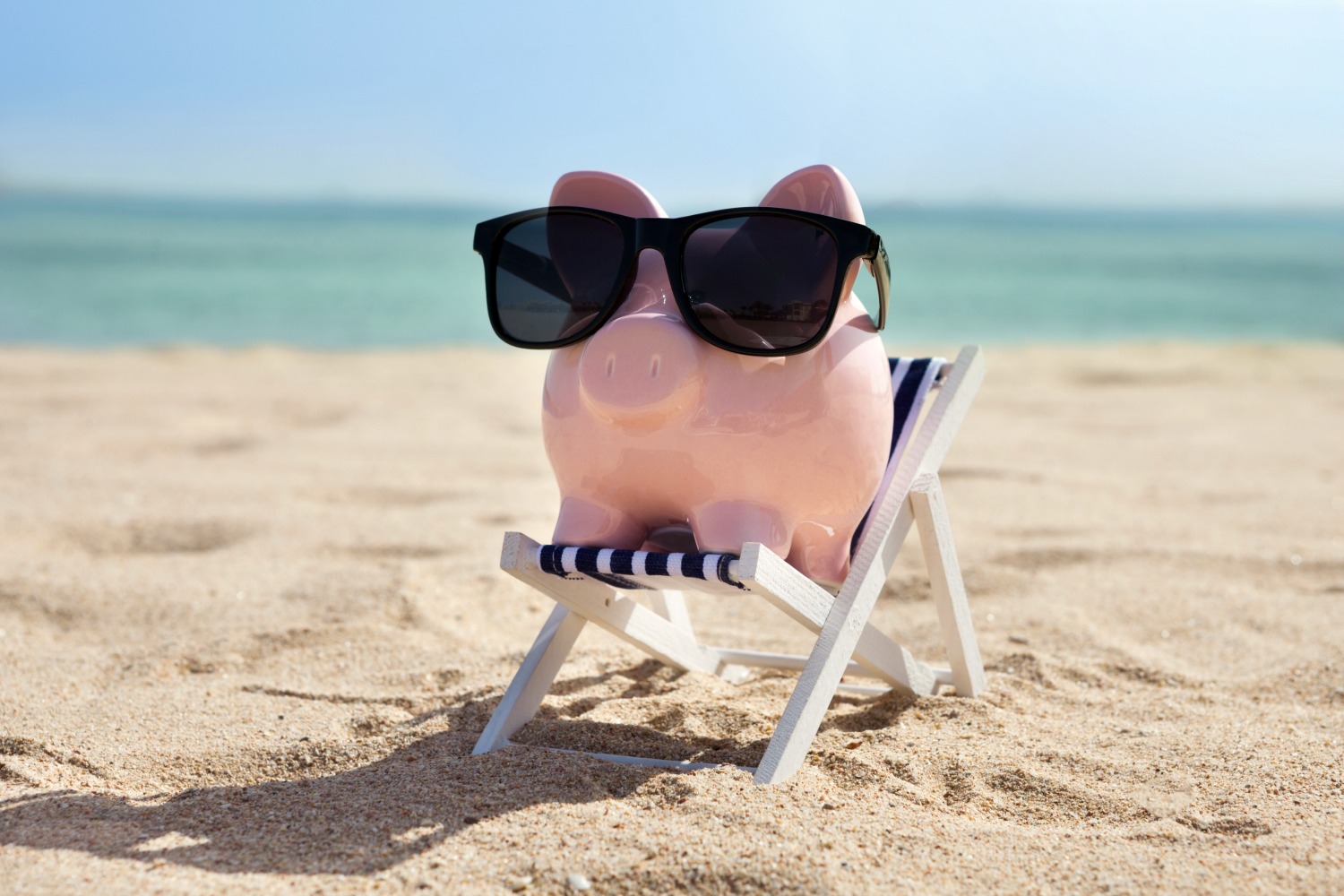 Piggy bank in sunglasses on a miniature deckchair on a beach - my Aruba tips including which currency to pack for Aruba