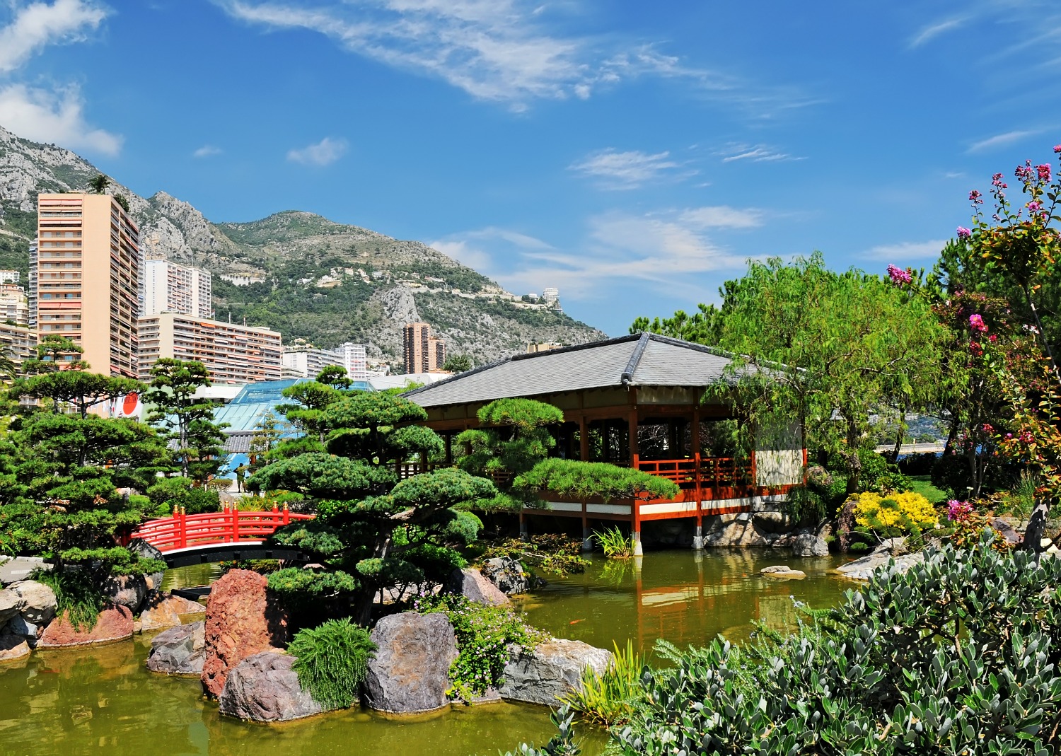 A view of the Japanese gardens in Monaco with buildings and mountains in the distance - a perfect place to escape the crowds if you're visiting Monaco with kids