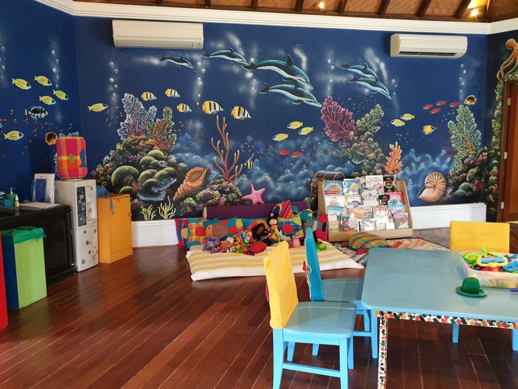 Table and chairs plus toys in front of a TV and walls decorated with fish at the kids club at Kuda Huraa, one of the Four Seasons Maldives resorts