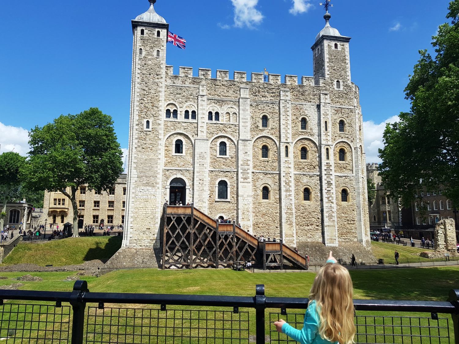 My daughter points up at the White Tower in the Tower of London with blue skies in the background