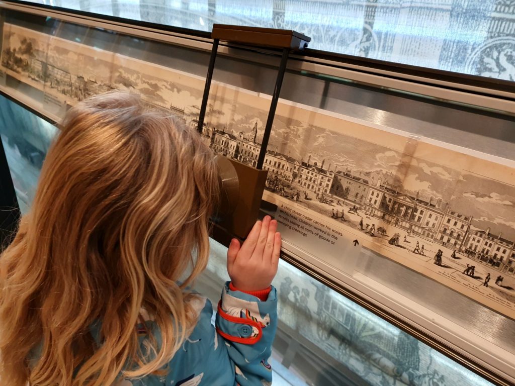 My daugher peers through a magnifying glass at a scene of historic London at the London Transport Museum