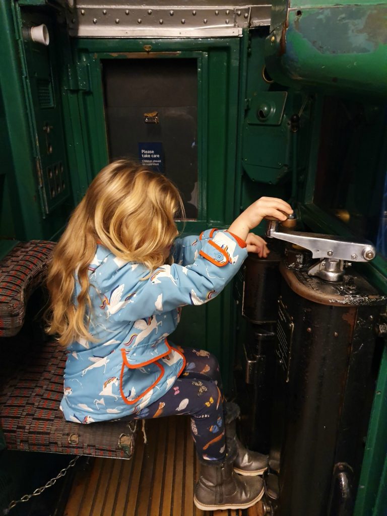 My daughter in the driver's seat of a tube train operating the dead man's handle at the London Transport Museum