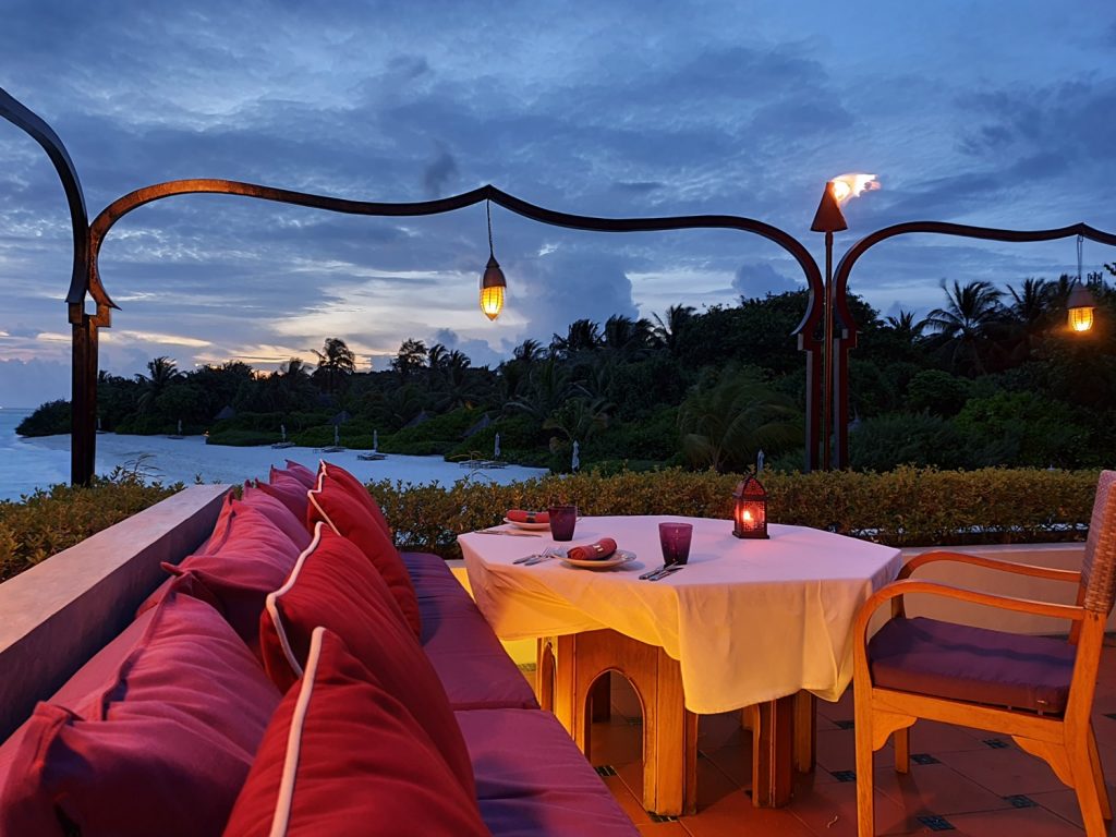 View from our table at Al Barakat restaurant in the Four Seasons Maldives resort Landaa Giraavaru after sunset, looking across the cushions to little lights and the water