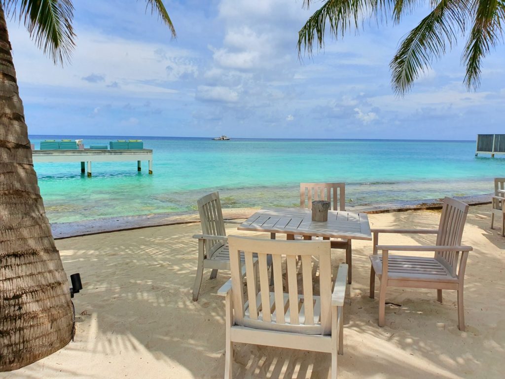 Chairs and tables on the beach at Fuego Grill restaurant at Four Seasons Maldives Landaa Giraavaru, with the turquoise Indian ocean in the background