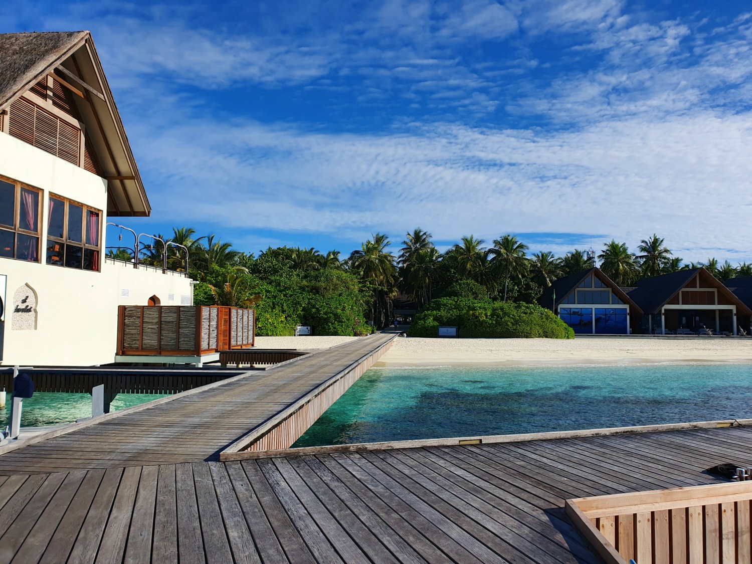 Jetty at Landaa Giraavaru resort in the Maldives with turquoise sea and white sand before the trees and buildings of the Four Seasons resort