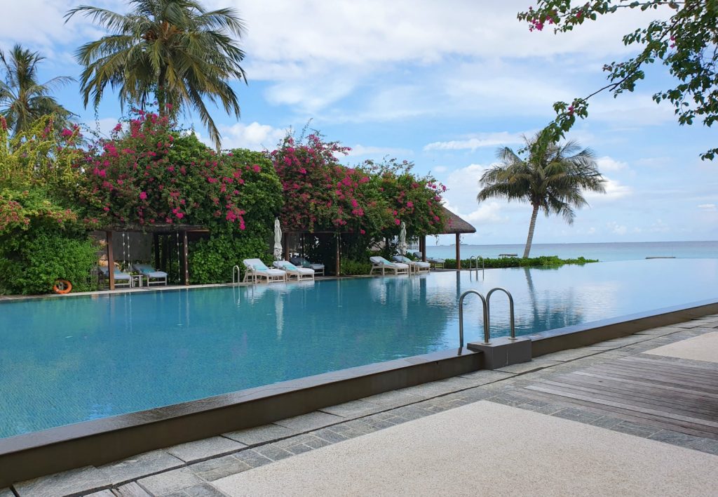 Looking across the infinity pool at Landaa Giraavaru resort in the Maldives, with loungers among the cabanas