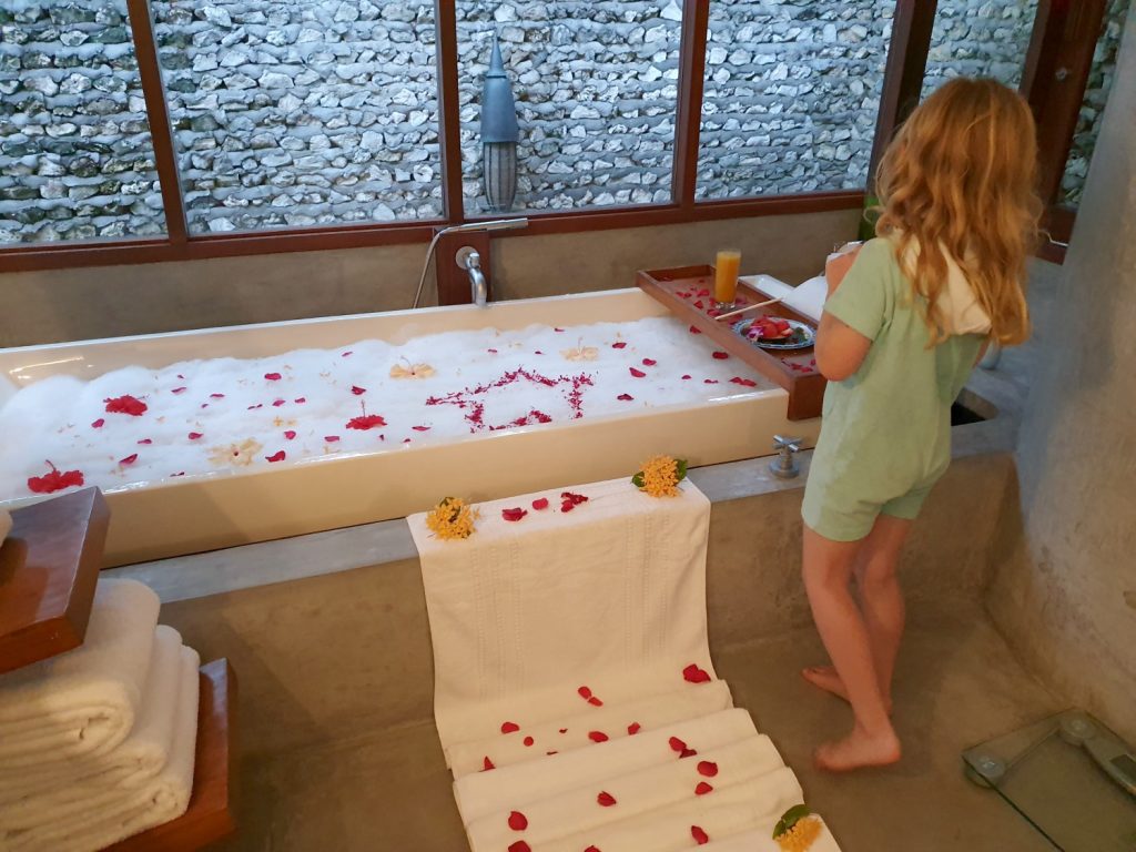 My daughter stands by the side of her special bubble bath with flower petals floating in the bubbles at Four Seasons Maldives resort Landaa Giraavaru