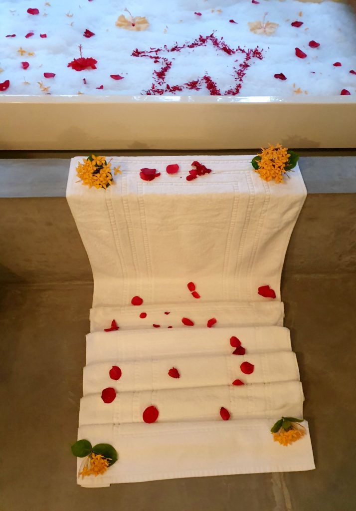 Folded towel scattered with flower petals leading up to a bubble bath with more flower petals including a star shape as a treat for my daughter at Landaa Giraavaru resort in the Maldives