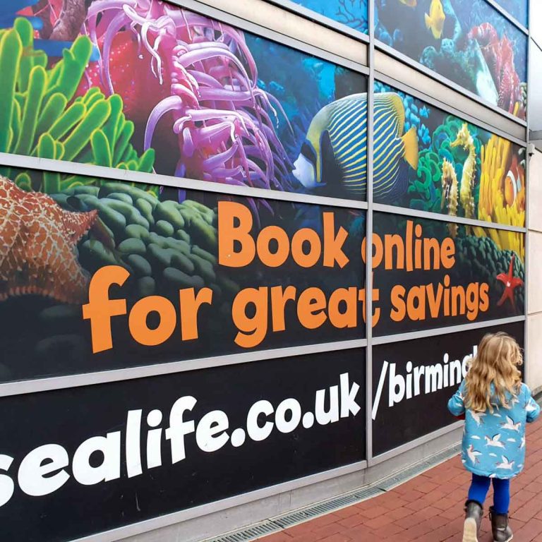 My daughter walks past the brightly coloured sign at the entrance to the Birmingham aquarium in Brindleyplace - my Birmingham Sealife Centre review