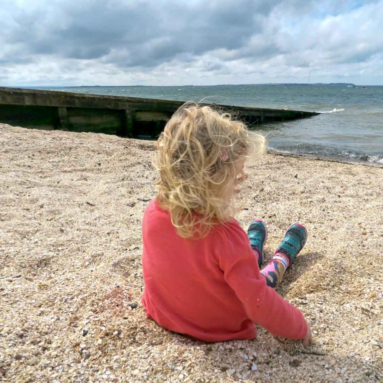 Girl relaxing on the shingle beach at Whitstable looking out to the sea on the Kent coast - my tips from our trip for Whitstable with kids