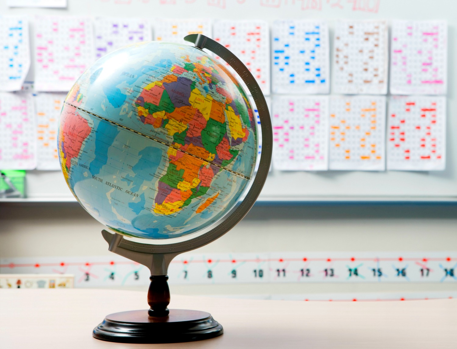Globe on a desk with school work on the wall behind - geography activities and quizzes to do from home in my virtual travel guide