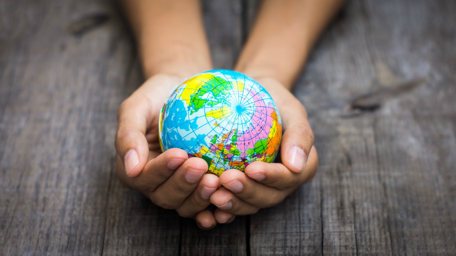 A person holding a globe on wooden background - my virtual travel guide with ideas for what families can do at home