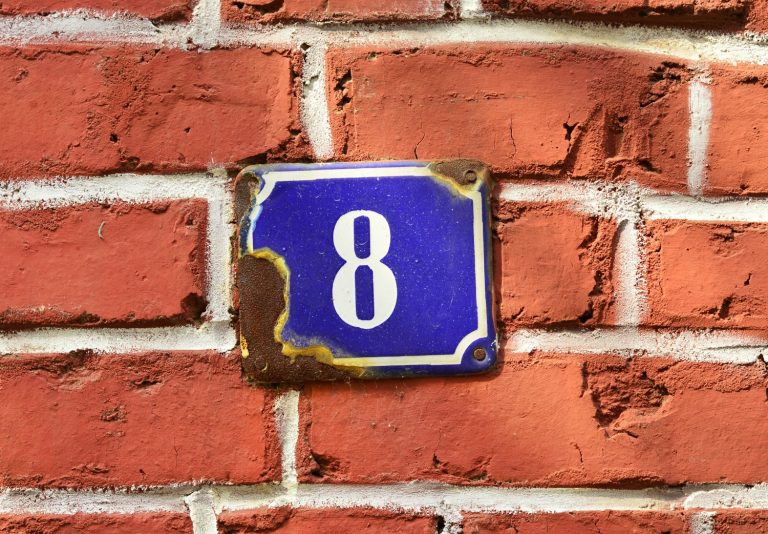 Blue number eight sign on a red brick wall, as I look back over eight years of travel with a child