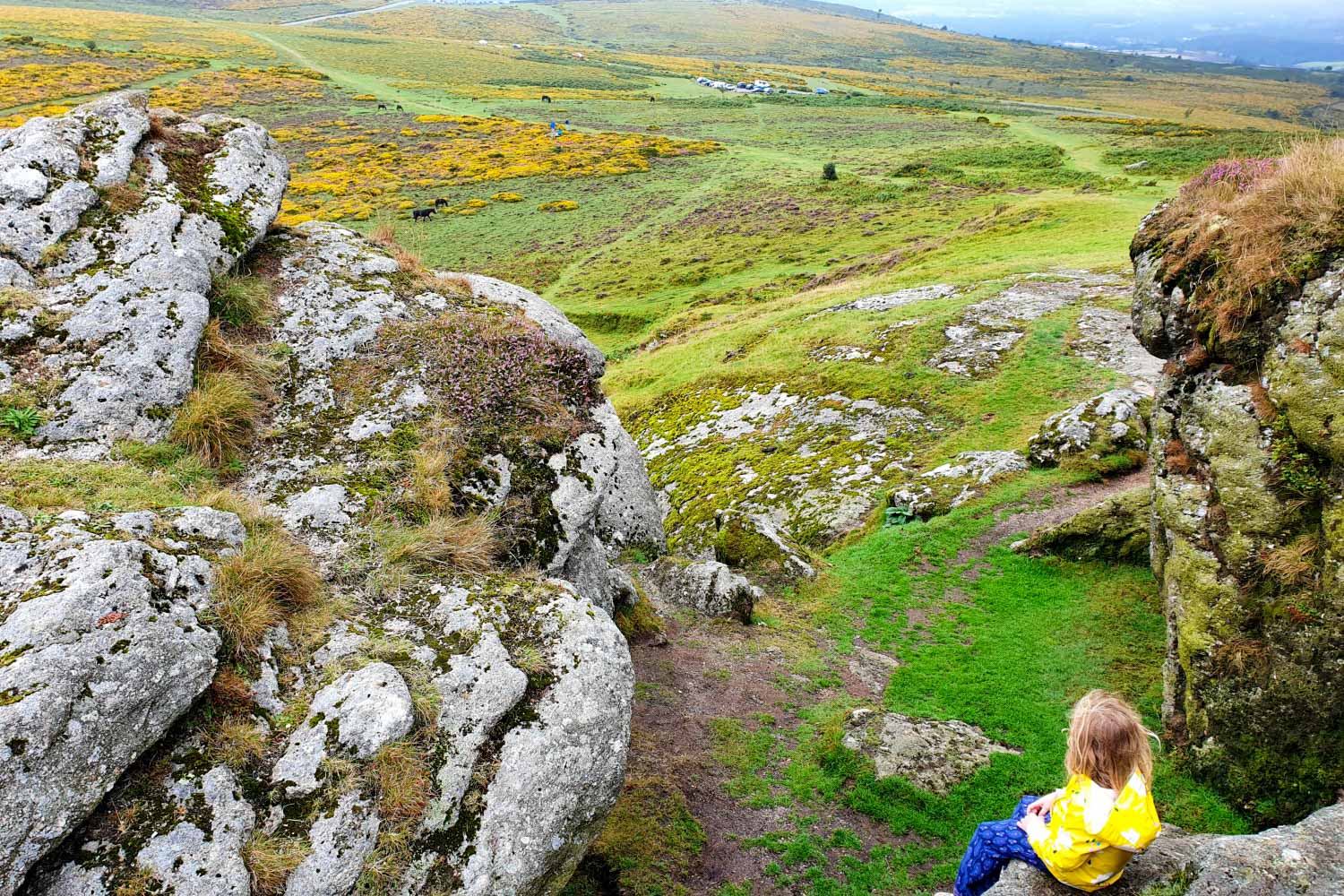 My daughter sits on the rocks by Saddle Tor looking down on to Dartmoor - you can't visit Dartmoor with kids without visiting at least one tor