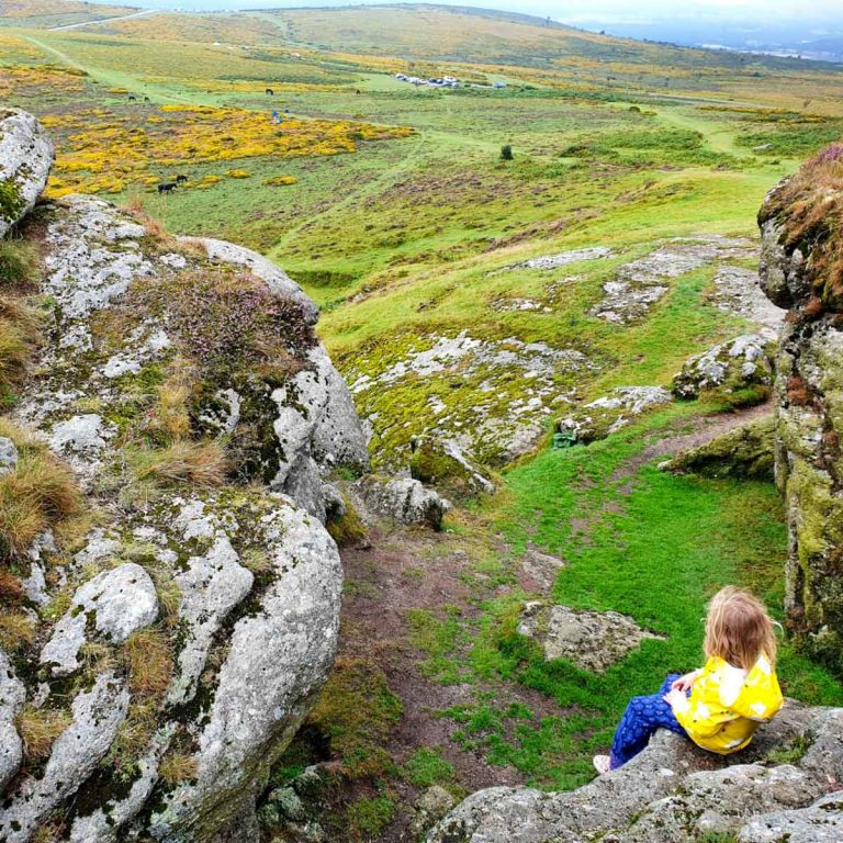 My daughter sits on the rocks by Saddle Tor looking down on to Dartmoor - you can't visit Dartmoor with kids without visiting at least one tor