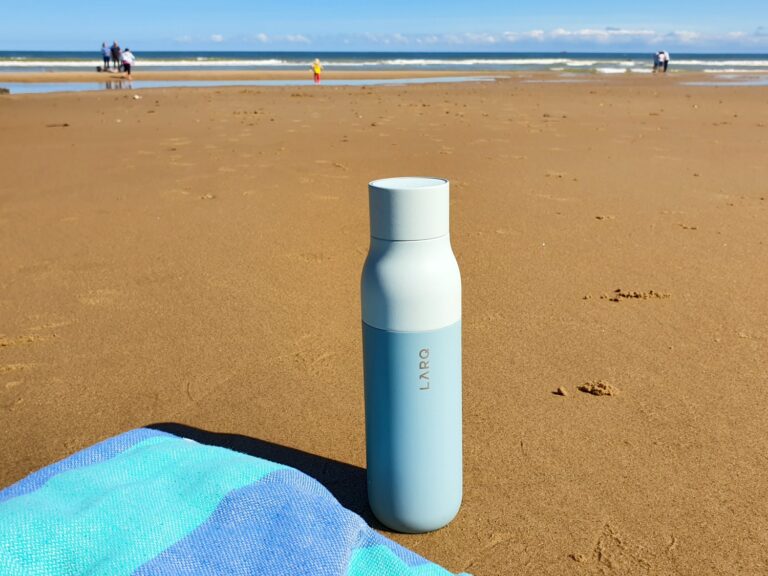 View of a pale blue Larq self-cleaning and purifying bottle next to a turquoise and blue hammam towel on the beach in the UK - my Larq bottle review