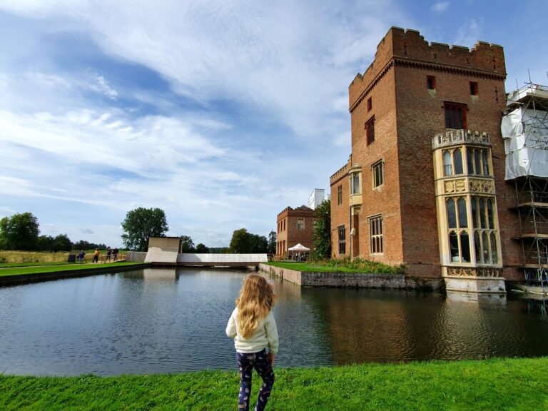 My daughter looks across the moat at part of Oxburgh Hall in Norfolk, undergoing a major renovation project, but still one of the best places to visit with kids in Norfolk