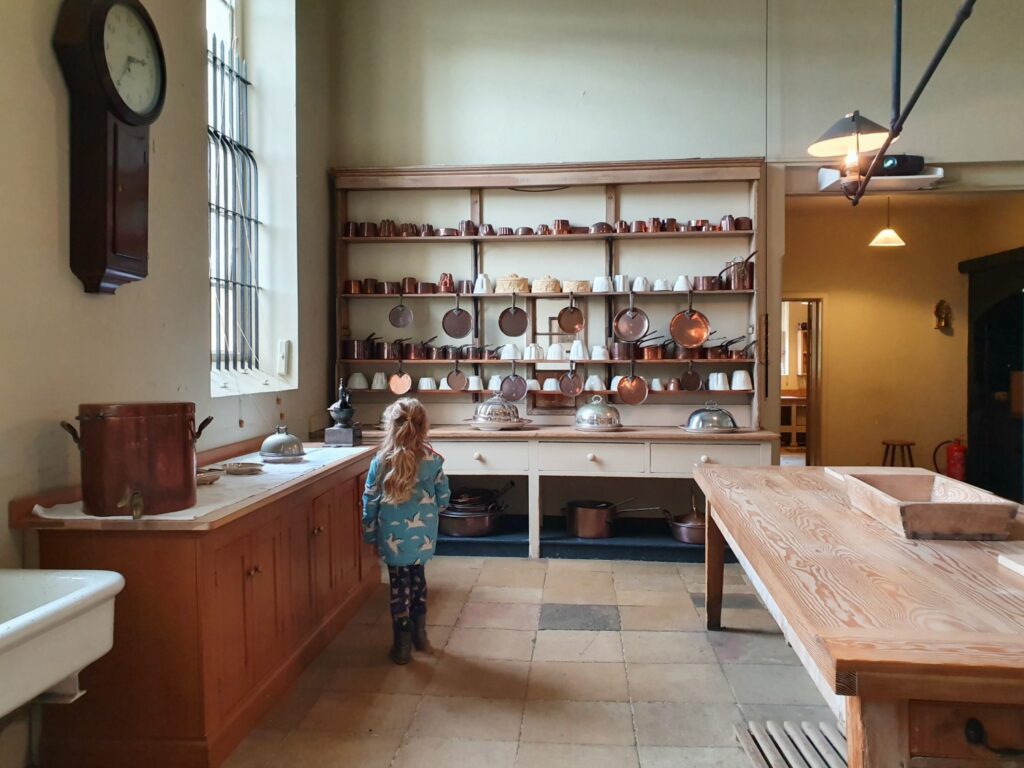 My daughter in the old kitchens looking at rows of pans at Audley End in Essex during a weekend in Saffron Walden with kids