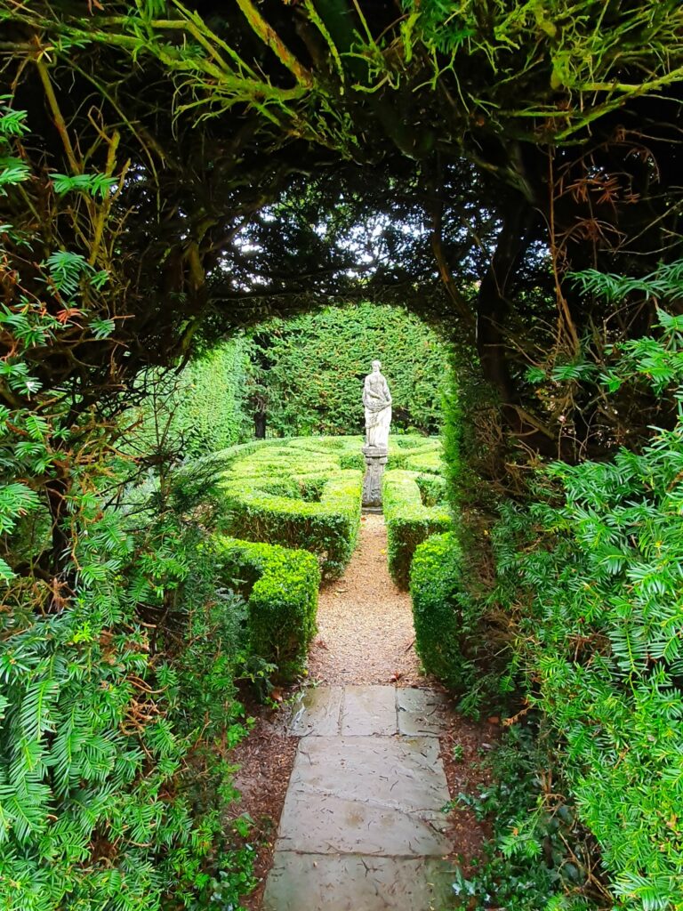 View to a statue through a hedge arch at Bridge End Gardens in Saffron Walden, a great place to get outdoors during a weekend in Essex with kids