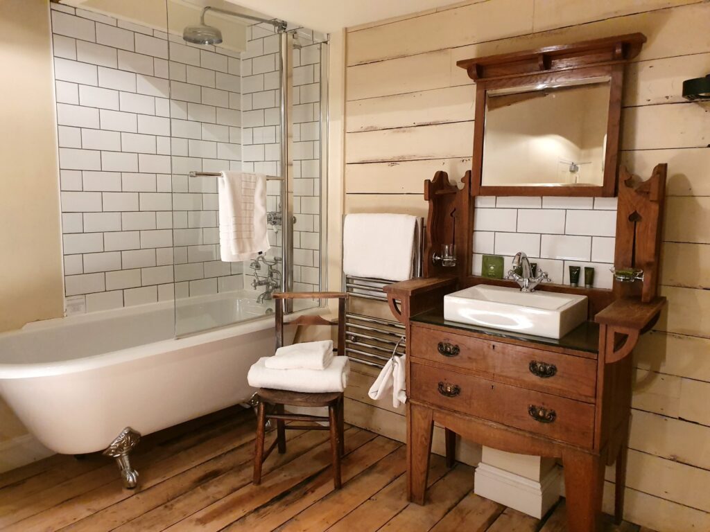 View of the bathroom within our room at the Cross Keys in Saffron Walden, Essex, including a claw foot bath with rainhead shower above