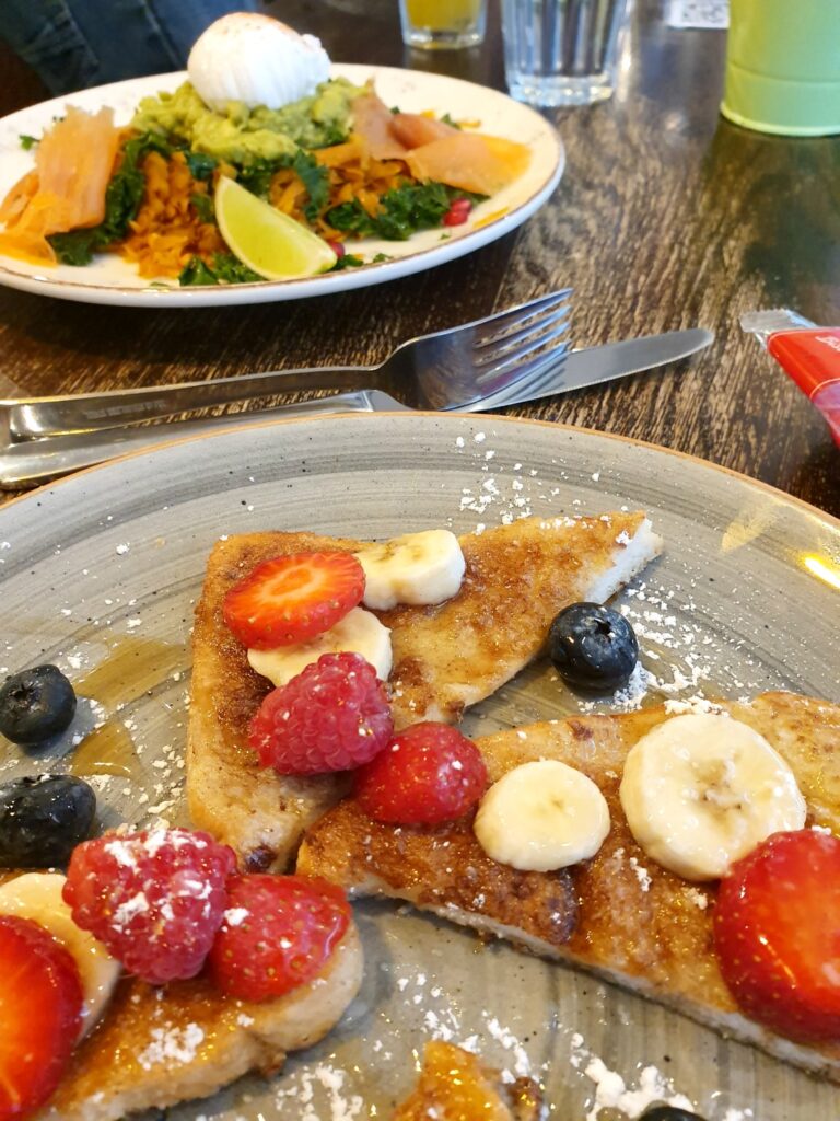 French toast with fruit and other brunch dishes in the background at the Curious Goat, one of the best places to eat in Saffron Walden with kids