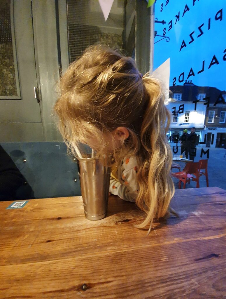 My daughter drinks her huge chocolate milkshake from a metal cup at Three Joes Winchester - one of my favourite places to eat in Winchester with kids