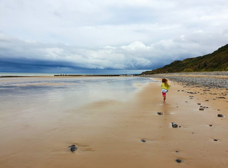 View of my daughter on the wide open empty beach between Cromer and Overstrand on a cloudy day, one of the part of the Norfolk Deep History Coast