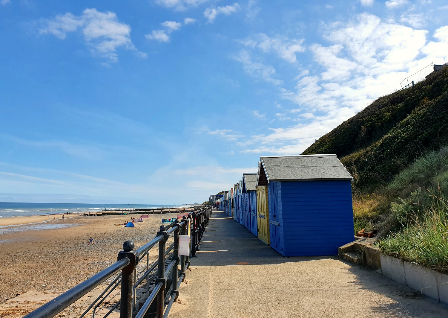 View along the promenade to small colourful beach huts and the flat beach leading to the sea at Mundesley in Norfolk