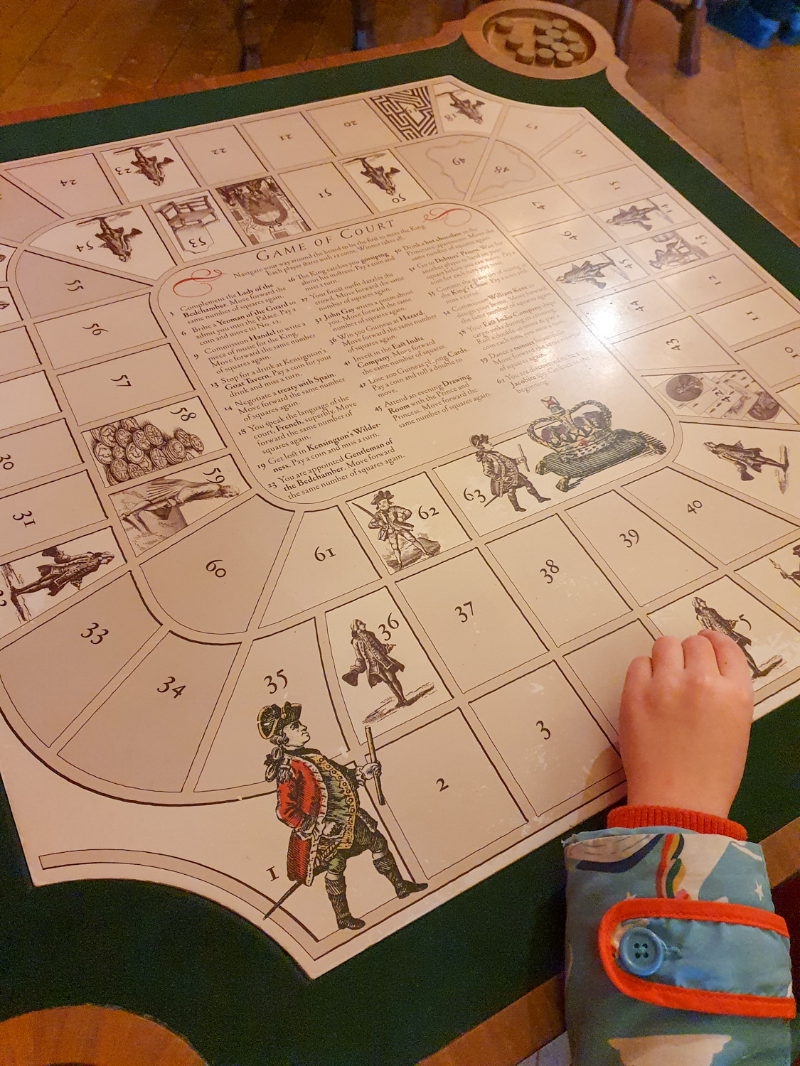 My daughter's hand reaching onto a board game for courtiers to move through life at court during a visit to Kensington Palace in London with kids