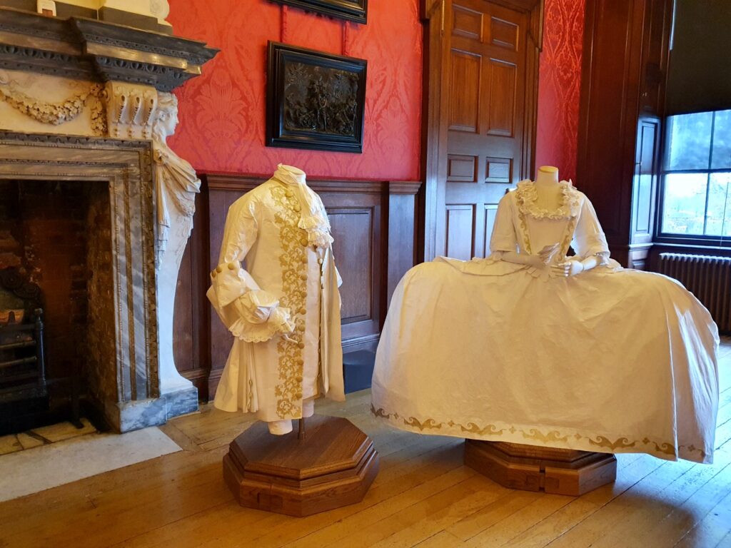 Recreation of court dress by a fireplace in a room with gaming tables at Kensington Palace