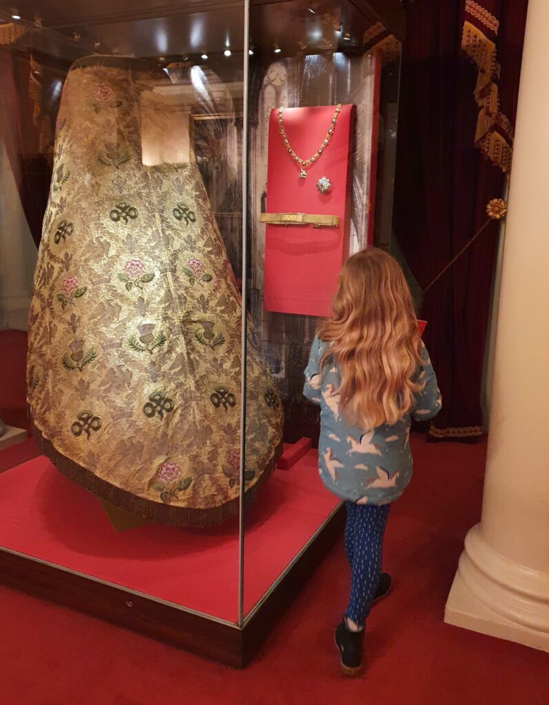 My daughter looks at a display of Queen Victoria's coronation regalia including the decorative cope during our visit to Kensington Palace with kids