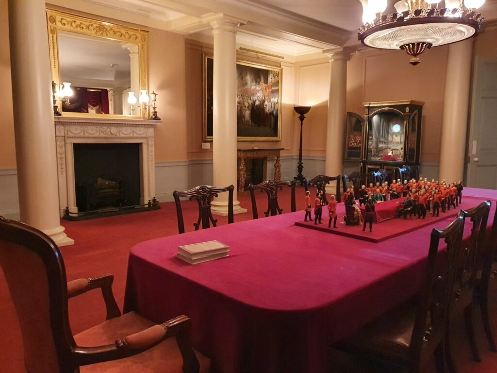 Recreation of Queen Victoria's first meeting with her privy council, with table and chairs set up and painting of the meeting in the background at Kensington Palace