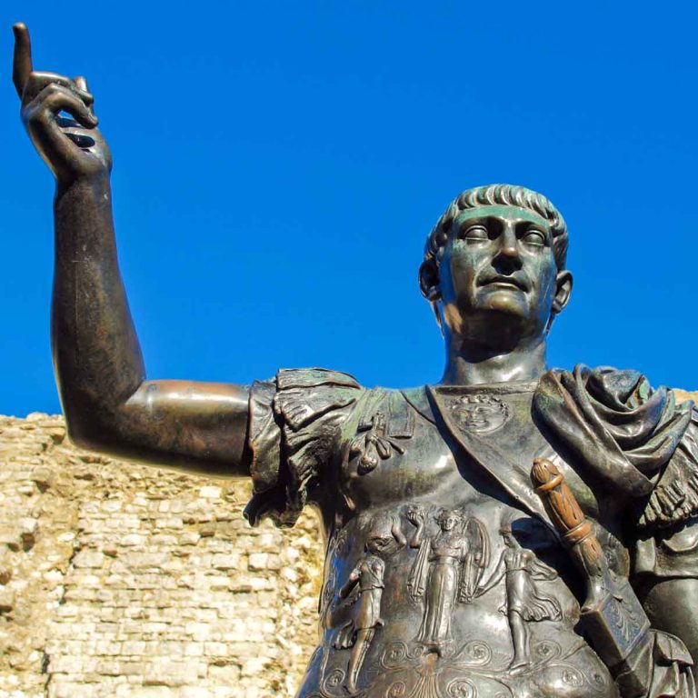 Statue with the head of the emperor Trajan in front of a section of Roman wall and blue sky in London - finding the best Romans sites in London