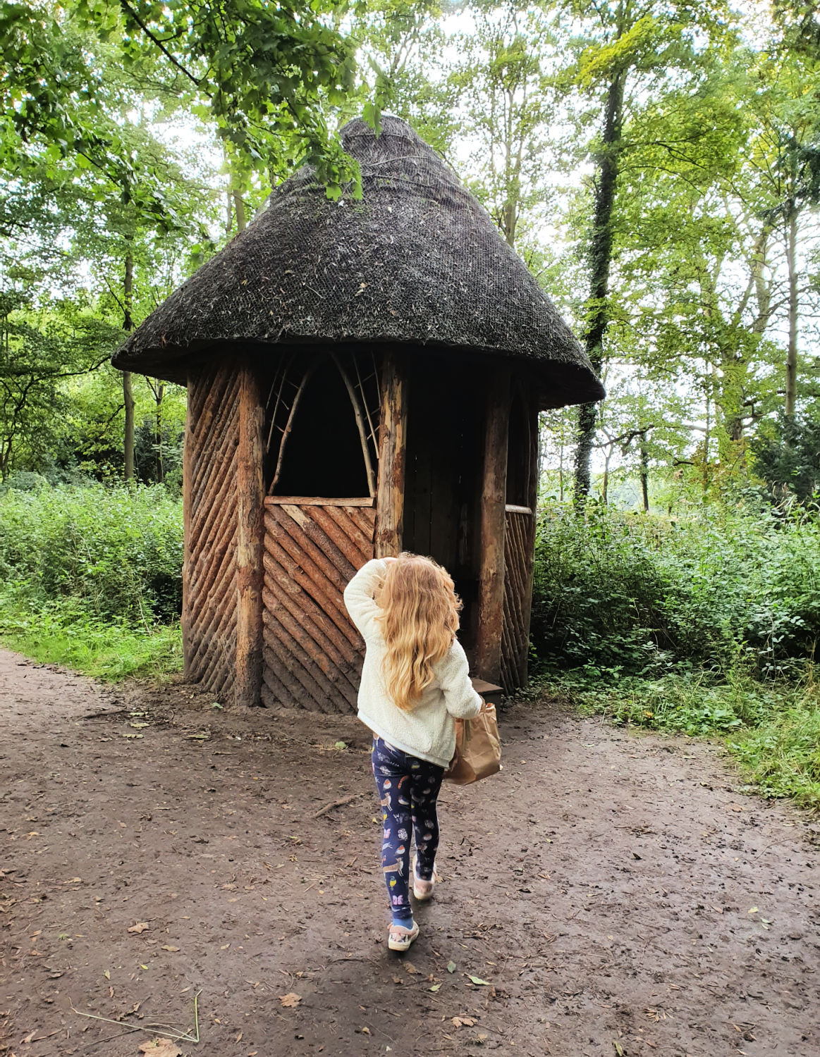 My daughter walks towards a little thatched hut in the woodland at Oxburgh Hall in Norfolk - a day out at Oxburgh Hall with kids