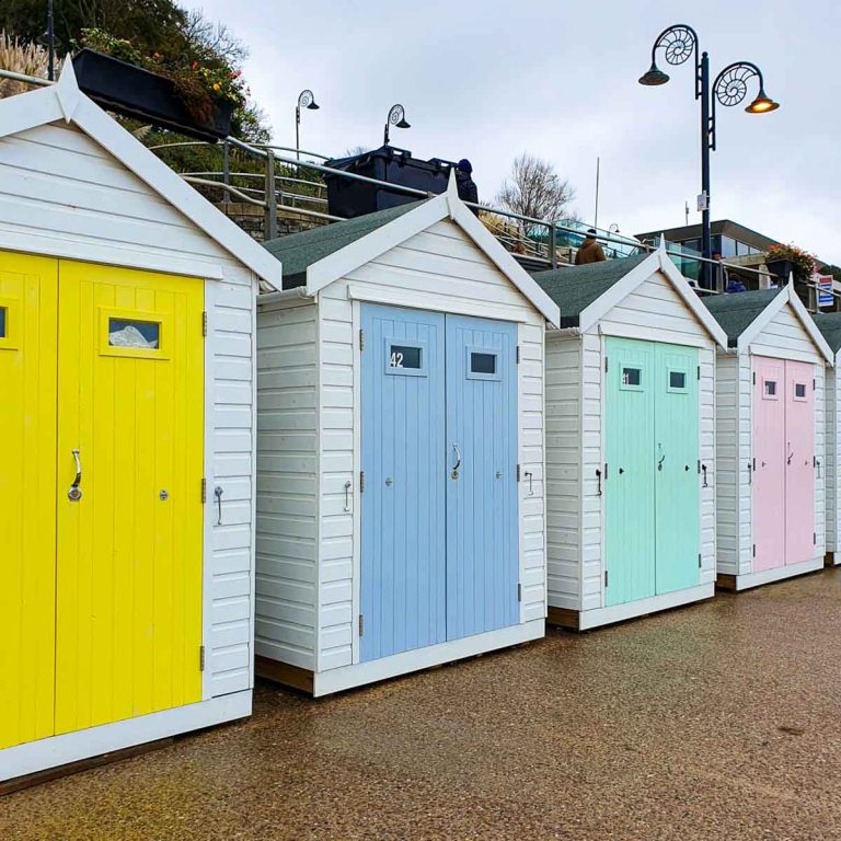 Row of brightly coloured beach huts on the beachfront at Lyme Regis in Dorset - discovering the best things to do in Lyme Regis with kids on a Dorset family holiday