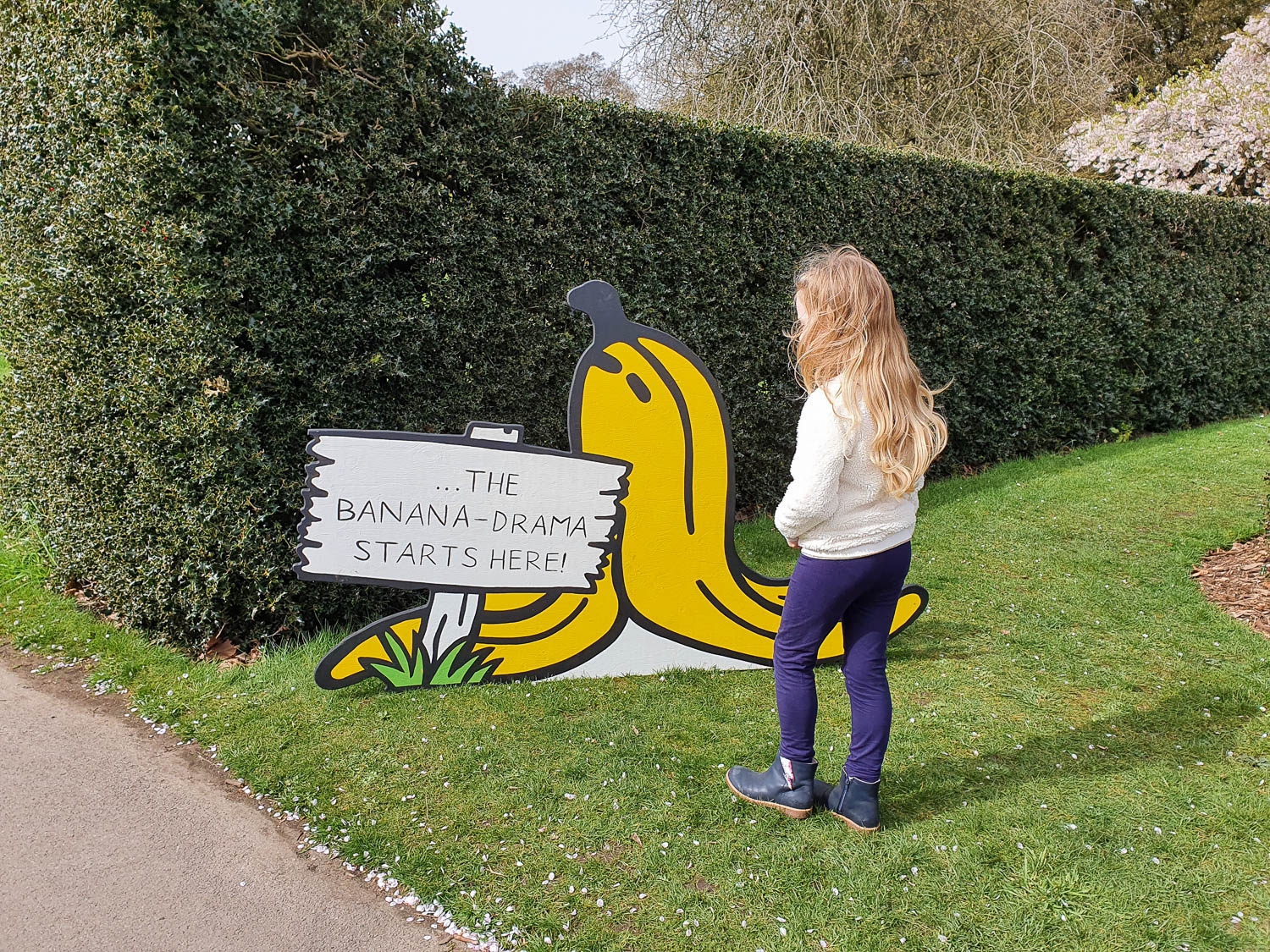My daughter with a sign saying the Banana Drama starts here, at the beginning of the kids trail for Easter at Kew Gardens