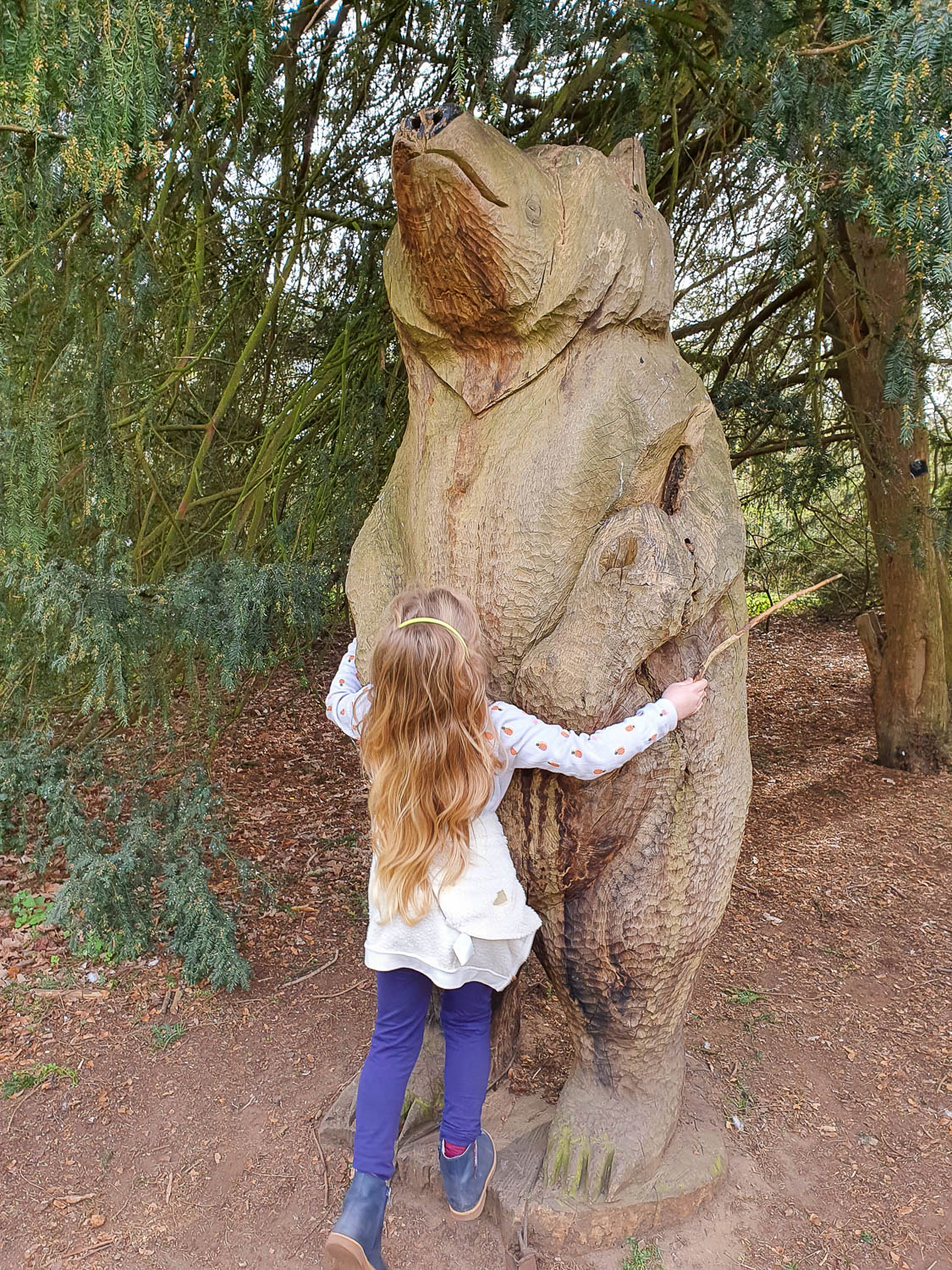 My daughter hugs a wooden statue of a bear at Kew Gardens - visiting Kew at Easter