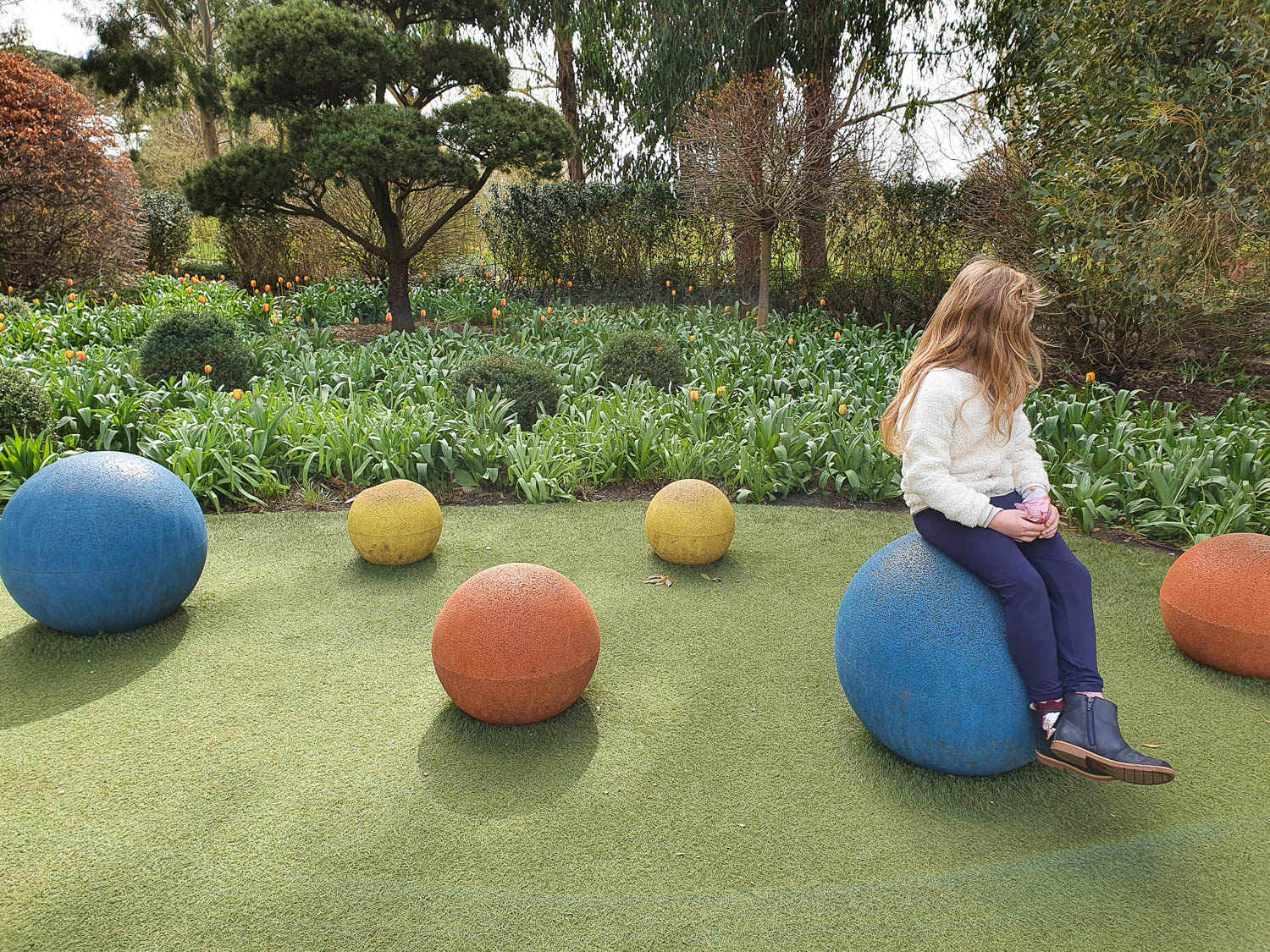 My daughter sits on one of the brightly coloured balls in the Children's Garden at Kew Gardens