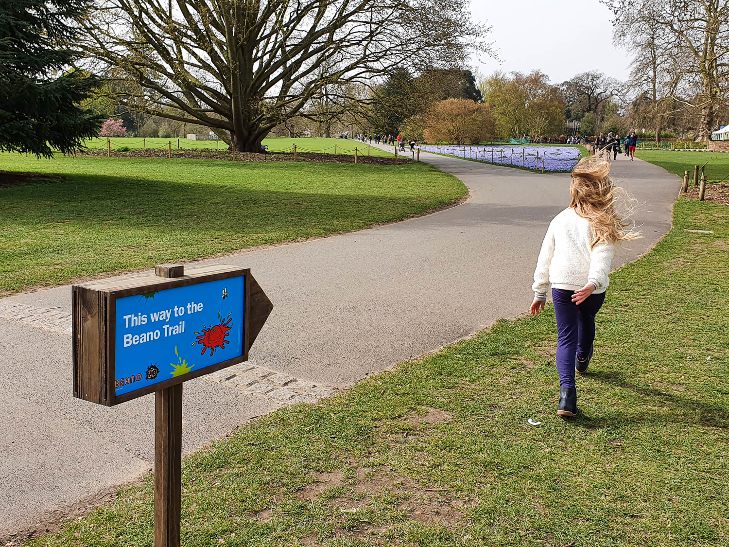 My daughter walks along a path with a sign showing the way to the start of the Beano trail at Kew Gardens - our family day out at Kew at Easter