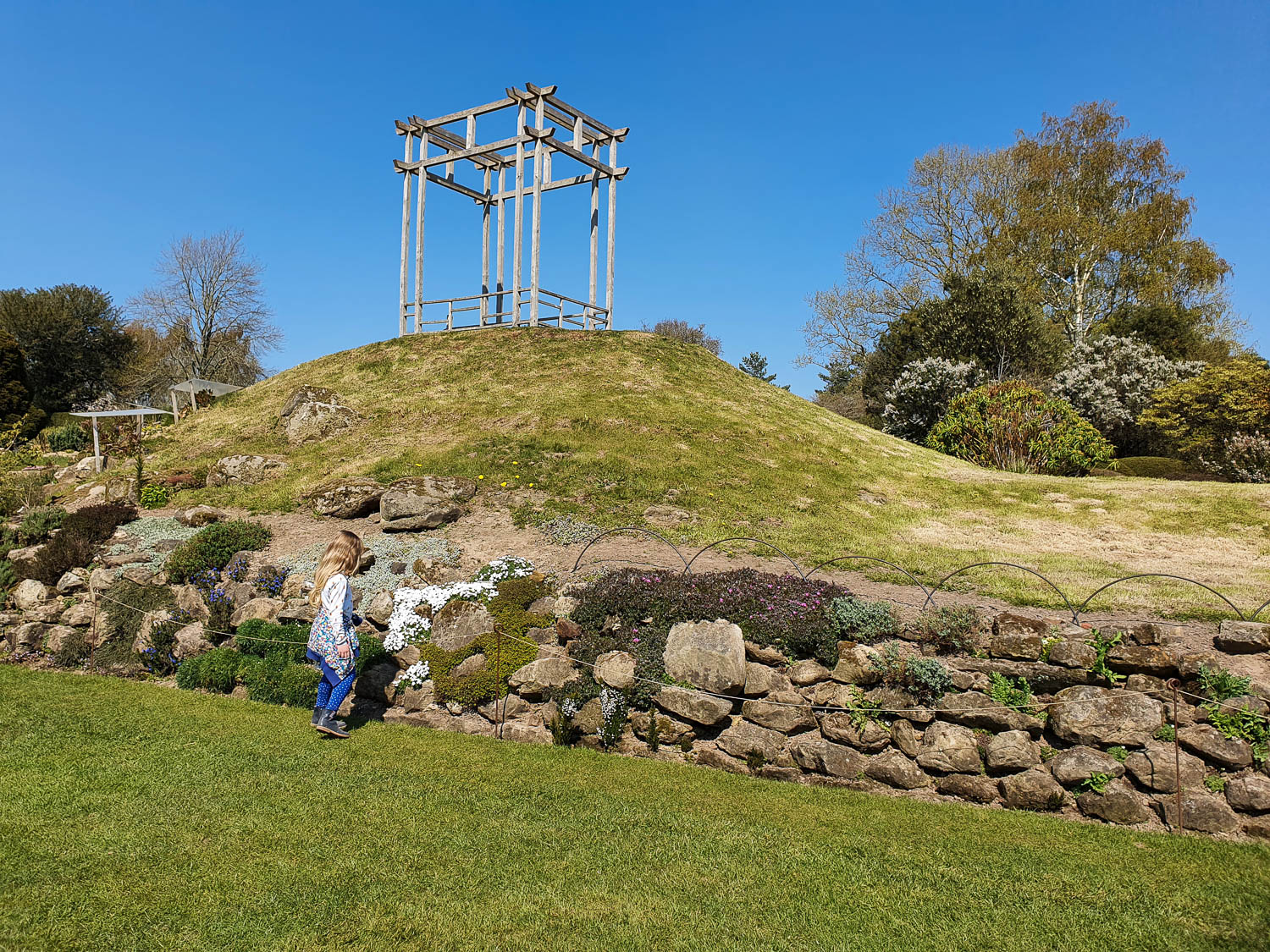 My daughter by plants in the rockery in one of the gardens at Nymans, a wooden structure above for a viewpoint - a day out with kids at Nymans in Sussex