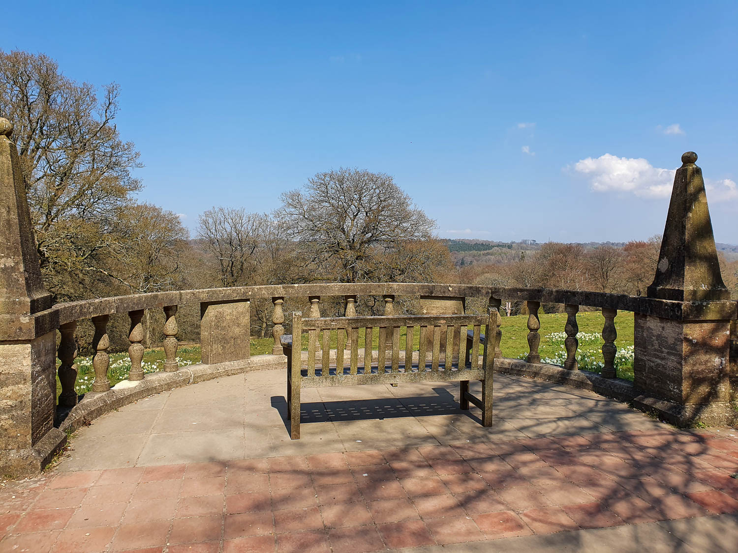 Bench in a semicircular viewpoint off the path at Nymans National Trust in Sussex with the countryside in the distance.