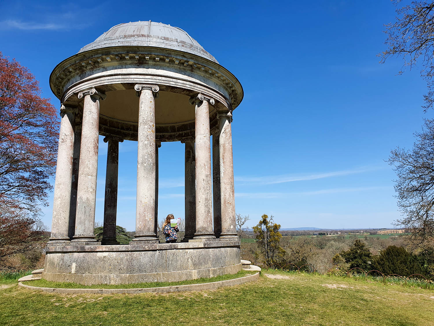 My daughter stands in the Doric temple at Petworth Park with a view out to the Sussex countryside - exploring Petworth with kids