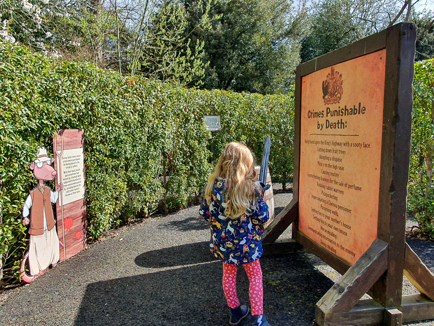 My daughter holds her toy sword while looking at a sign showing crimes punishable by death in Tudor times in the Horrible Histories Maze at Warwick Castle