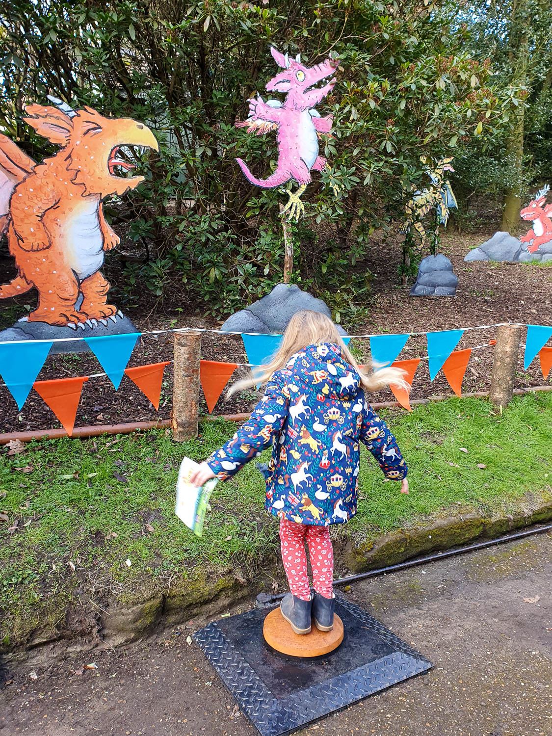 My daughter jumps on a foot-operated pad to make dragon roars, with cut-outs of characters from the book Zog by Julia Donaldson in the background - my review of the Warwick Castle Zog trail, Zog and the Quest for the Golden Star