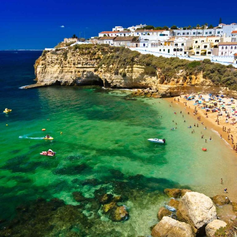 Looking out onto the beach and pretty buildings of an Algarve town on the rocky cliffs over the clear green sea - one of my top reasons for visiting Portugal with kids