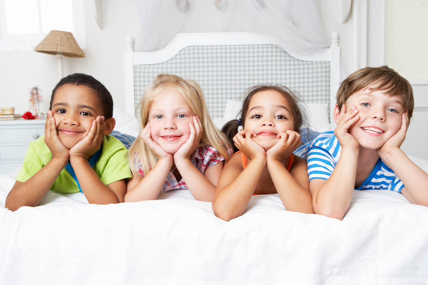 Four happy kids lying on a white duvet on a bed smiling - if you're wondering where to stay in London with kids, I've picked out the best family hotels in London in my guide to London with kids