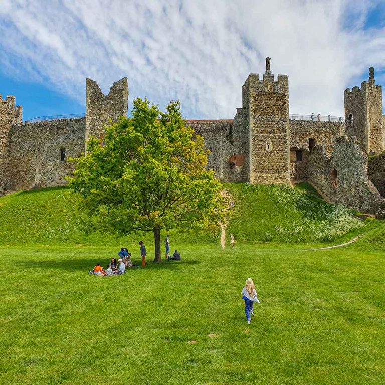 My daughter runs towards Framlingham Castle on its hill, with its stone towers and some crumbling walls - visiting Framlingham Castle with kids