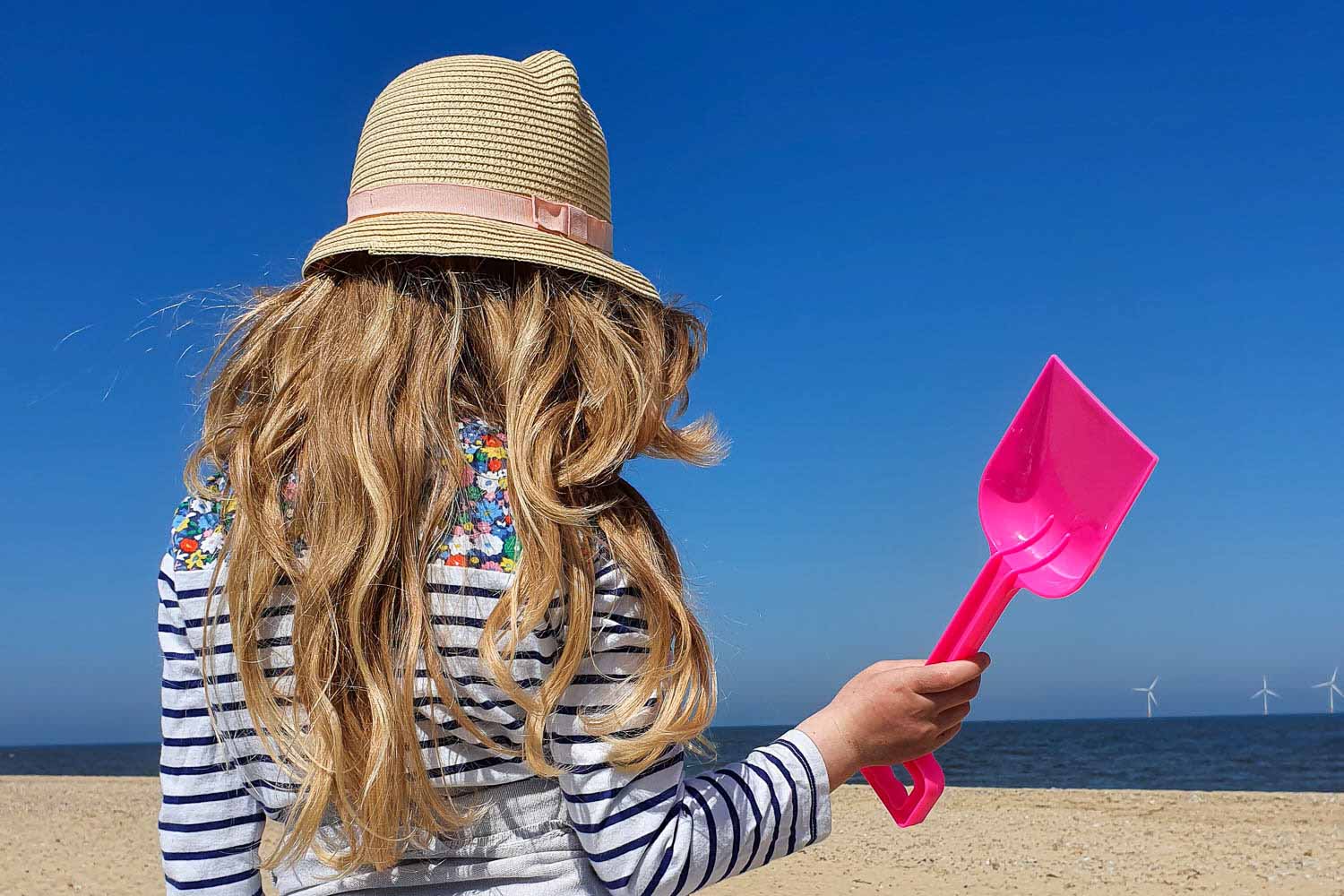 My daughter wearing a sunhat on a beach in Norfolk holding a bright pink spade - my pick of the best beaches in Norfolk with kids