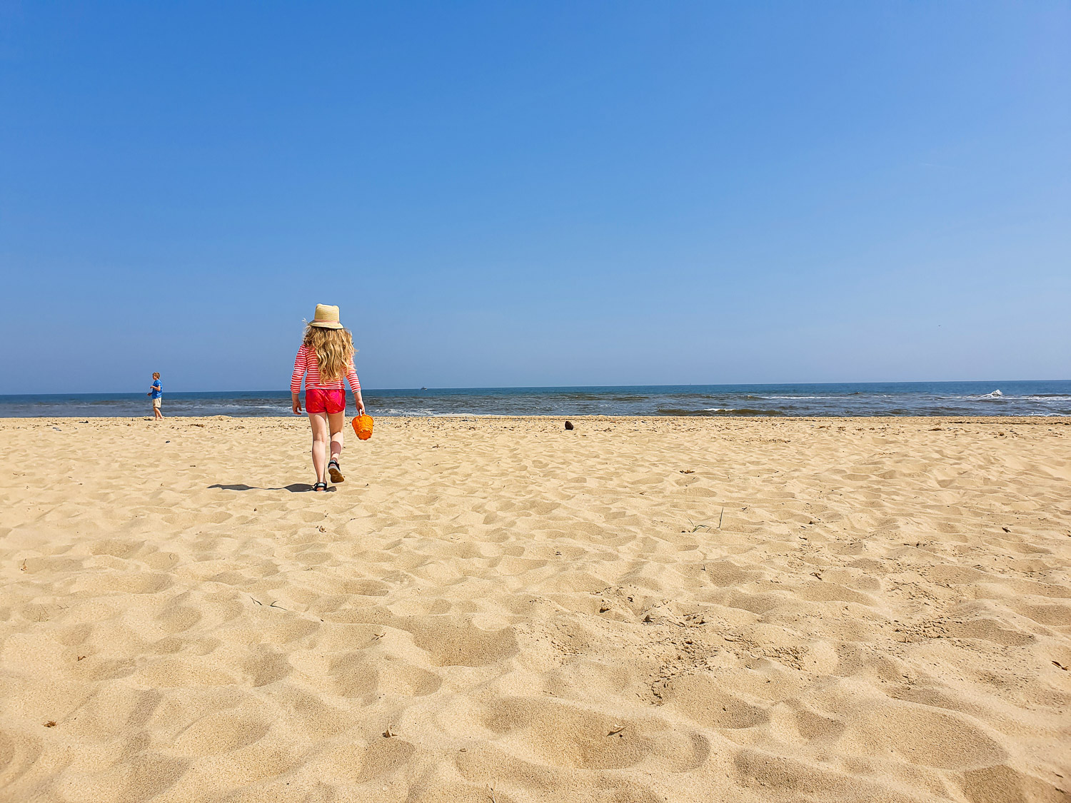 My daughter with bucket walking across the sand towards the waves at Winterton-on-Sea beach, one of my favourite beaches with kids in Norfolk