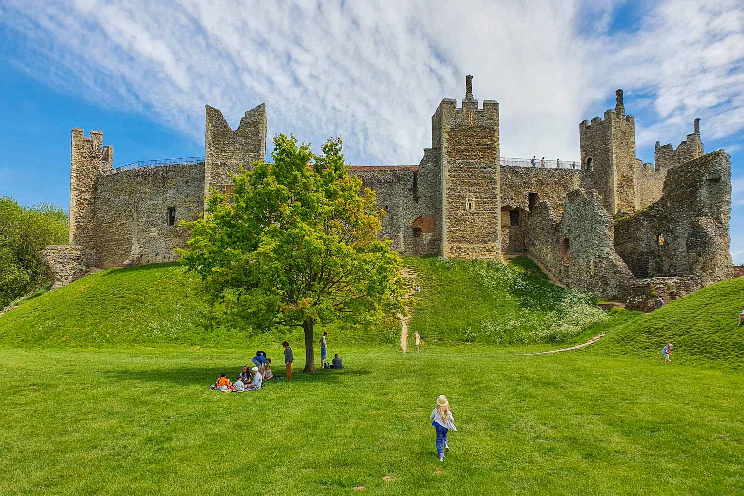 My daughter runs towards Framlingham Castle on its hill, with its stone towers and some crumbling walls - visiting Framlingham Castle with kids